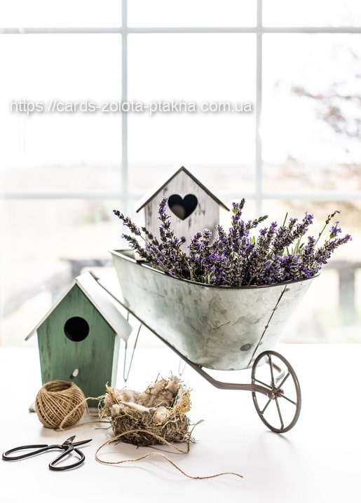 Miniatur-Schubkarre mit Lavendel neben zwei Holz-Vogelhäuschen, Gartenschnur und einem Nest