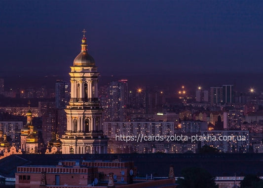 Golden-domed Great Lavra Bell Tower illuminated at dusk above Kyiv's lit-up city skyline