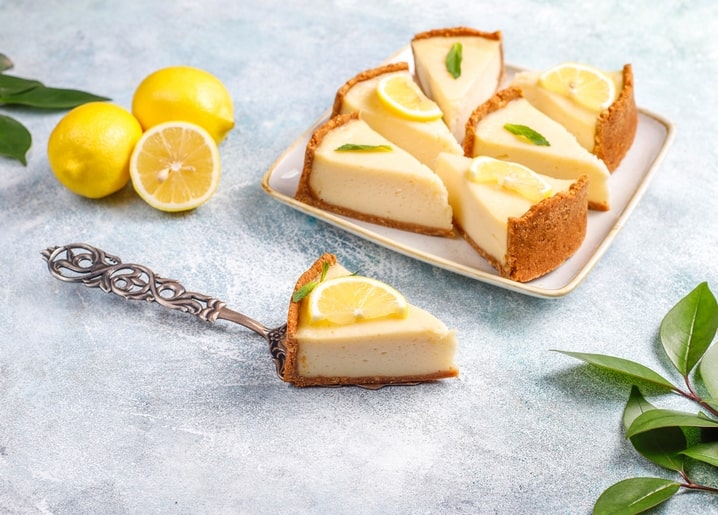 Aufgeschnittene Zitronen-Cheesecake-Tarte neben frischen Zitronen und einem Vintage-Tortenheber