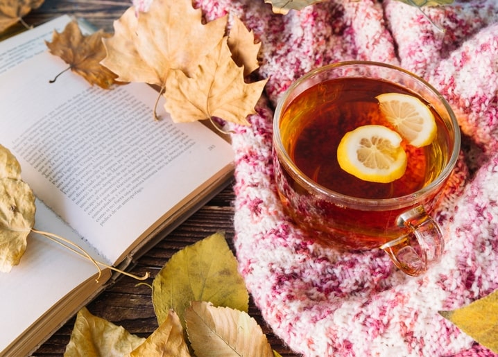 Cup of lemon tea beside an open book on a pink knit blanket with maple leaves