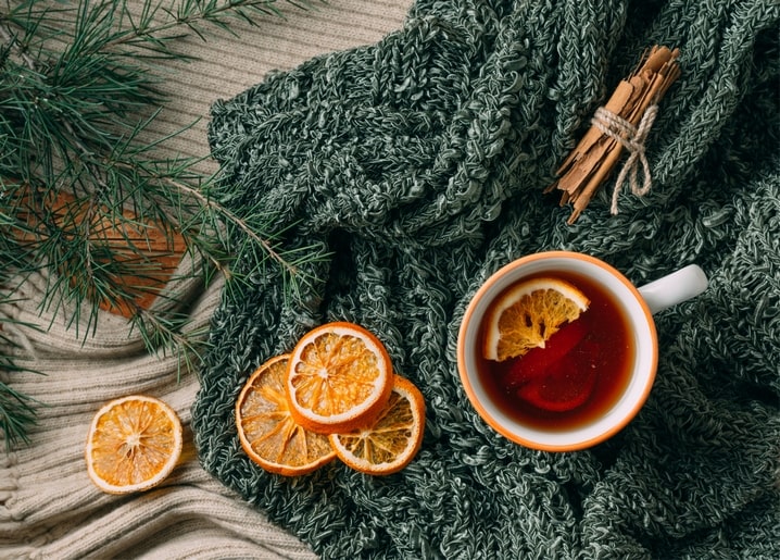 Tasse Zitronentee auf grüner Strickdecke mit Tannenzweigen, Orangenscheiben und Zimtstangen