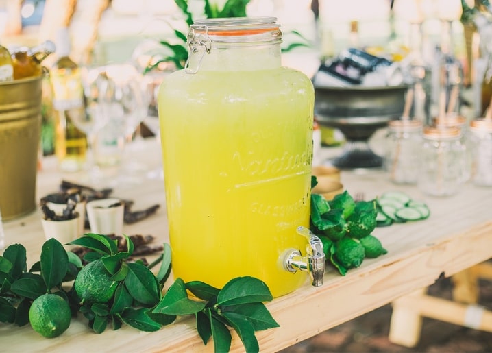 Glasspender mit Limonade und Zapfhahn zwischen frischen Limetten