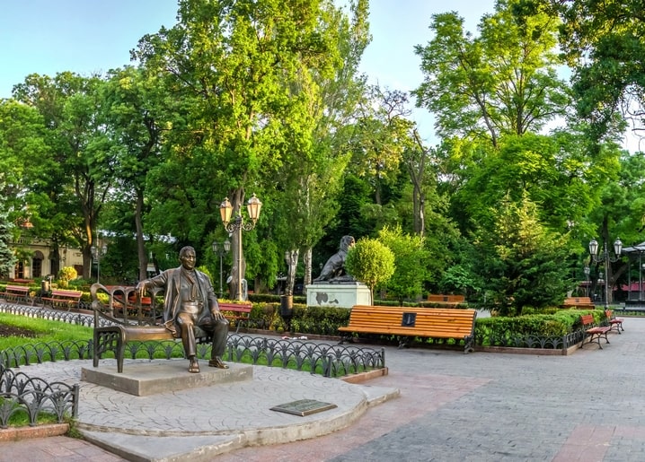 Бронзова статуя Леоніда Утьосова на лавці в Одеському міському саду, поруч статуя собаки
