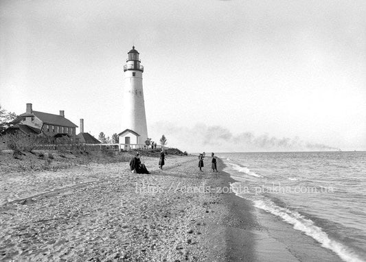 Schwarz-weiß-Foto eines Leuchtturms mit Frauen am wellenumspülten Strand
