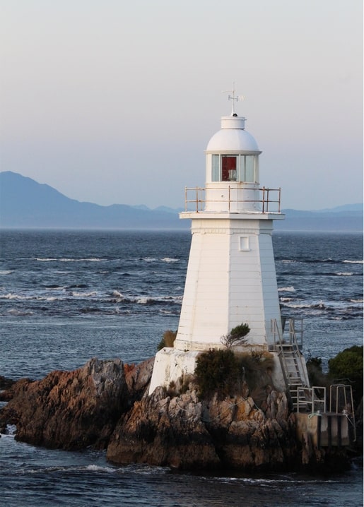 Weißer Leuchtturm auf einem Felsvorsprung über dem Meer bei Abenddämmerung