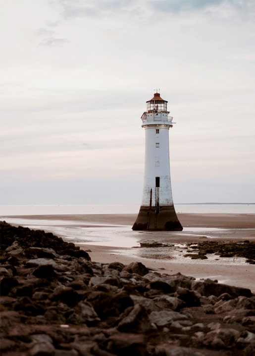 Weißer Leuchtturm an einem felsigen Strand bei Ebbe unter blassem Himmel