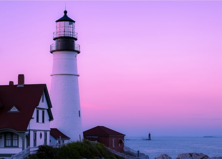Weißer Leuchtturm und Wärterhäuschen bei rosa Abenddämmerung am Meer