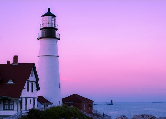 Weißer Leuchtturm und Wärterhäuschen bei rosa Abenddämmerung am Meer