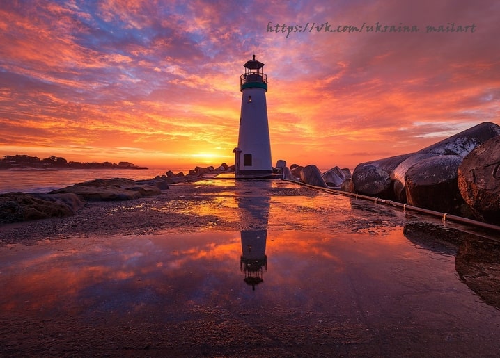 Weißer Leuchtturm vor feurigem Sonnenuntergang mit Spiegelung in einer Gezeitenpfütze