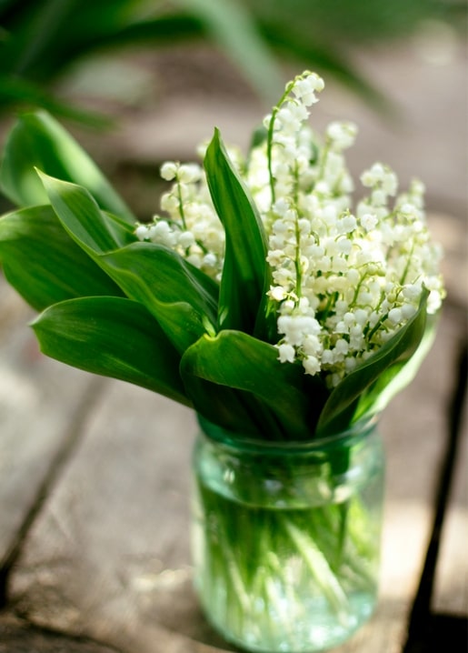 Lily of the valley bouquet in a glass jar on a rustic wooden table
