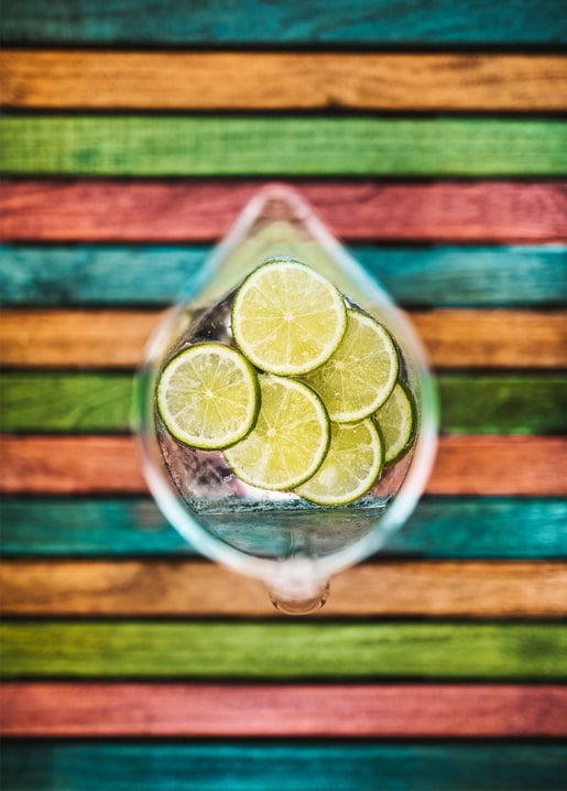In Scheiben geschnittene Limetten in einem Glas Wasser, von oben vor bunt gestreiftem Holz.