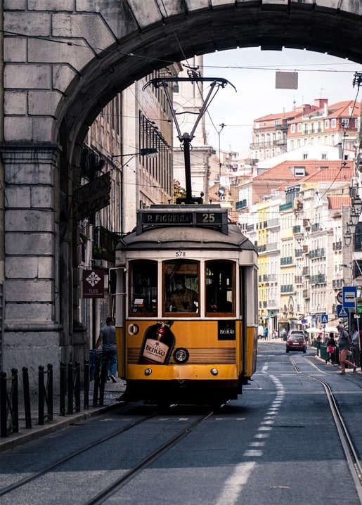 Vintage yellow tram passing under a stone archway on a cobbled Lisbon street