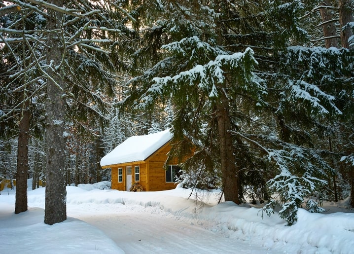 Small wooden cabin buried in snow among tall spruce trees in a winter forest