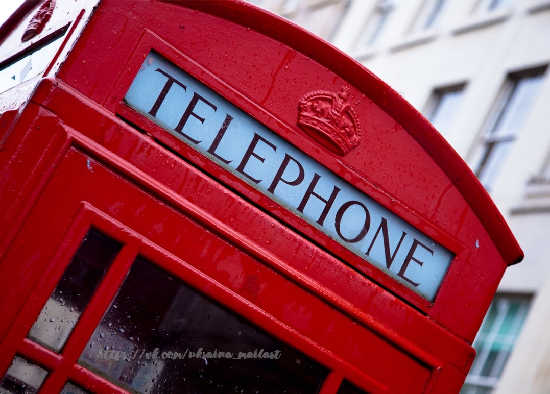 Nahaufnahme einer roten Londoner Telefonzelle mit Regentropfen und der Krone über „Telephone“