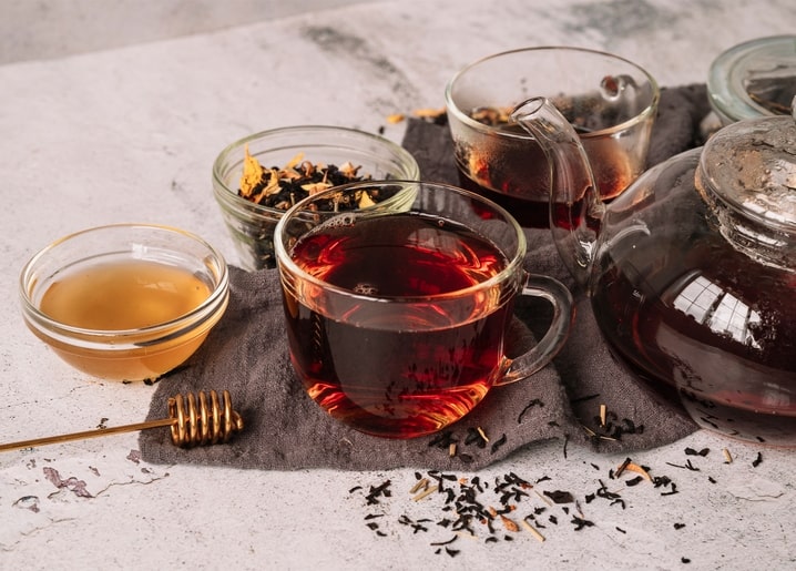 Glass teapot of tea with loose leaves, a bowl of honey and honey dipper on a linen cloth