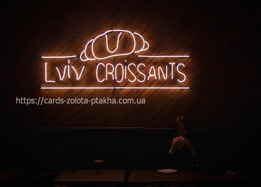 Neon sign reading 'Lviv Croissants' glowing above a café table at night