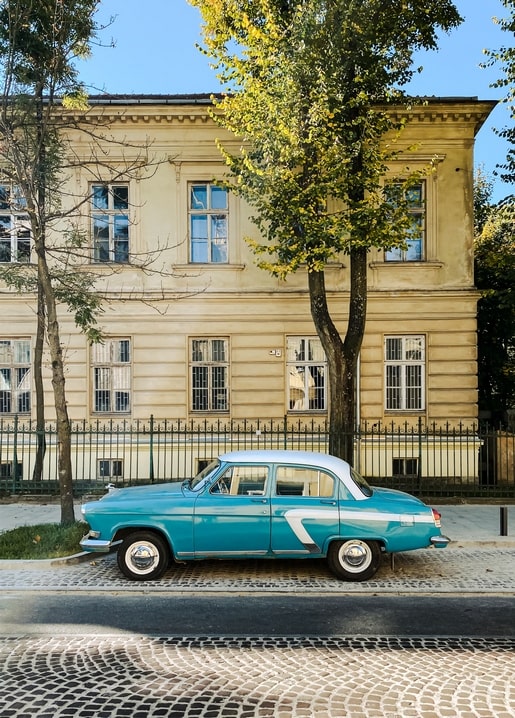 Türkisfarbener Oldtimer auf dem Kopfsteinpflaster vor einem historischen Gebäude in Lwiw