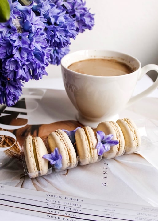 Row of macarons beside a latte and purple hyacinths on stacked Vogue Polska magazines