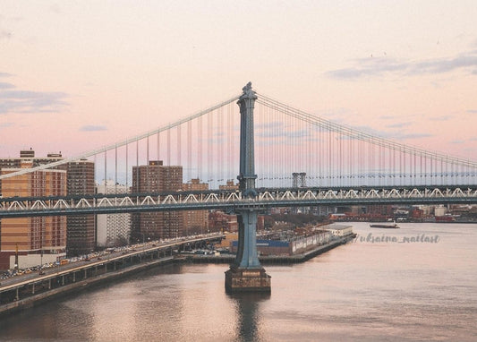 Die Manhattan Bridge vor rosafarbenem Abendhimmel über dem East River und der Skyline