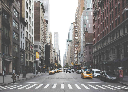 Gelbe Taxis überqueren eine breite Straße in Manhattan zwischen Wolkenkratzern