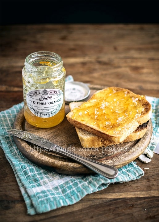 Glas Orangenmarmelade neben Toast und Messer auf einem rustikalen Holztisch