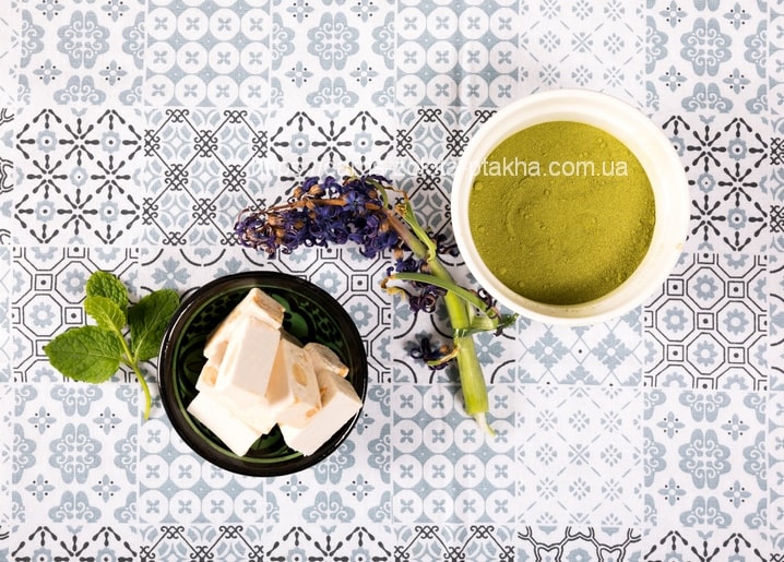 Bowl of matcha powder with tofu cubes, mint and dried allium flowers on tile