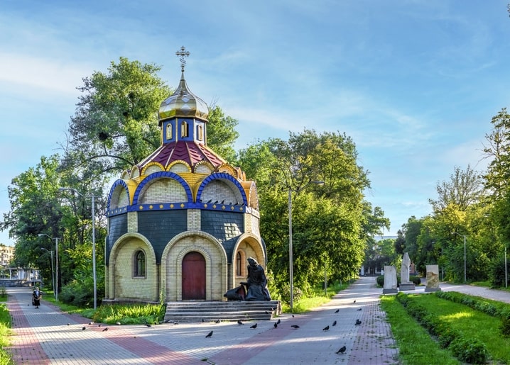 Каплиця з кольоровим куполом у парку Черкас, біля входу бронзова постать у скорботі