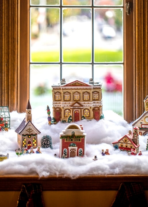 Miniatur-Weihnachtsdorf mit Rathaus, Kirche und Post in Watte-„Schnee“ auf der Fensterbank.