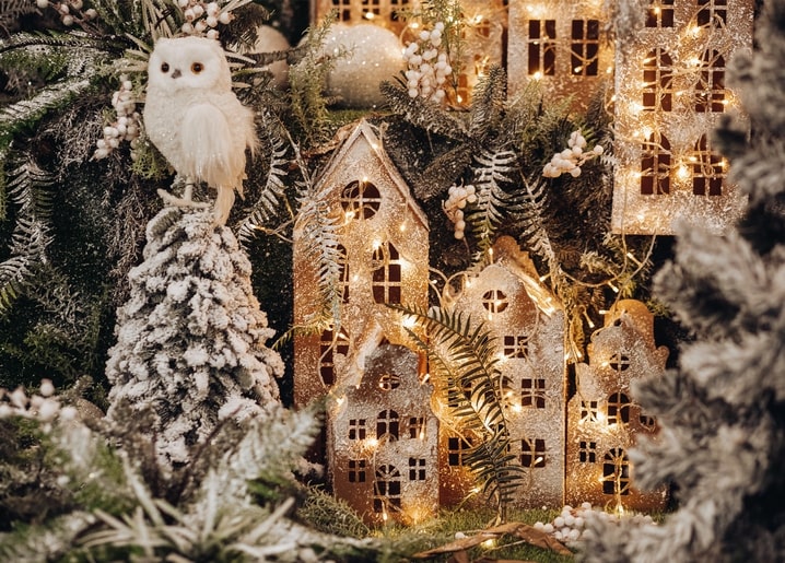 Winziges glitzerndes Weihnachtsdorf mit weißer Eulenfigur auf einem verschneiten Zweig