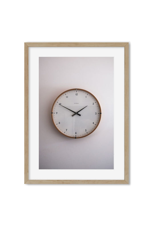 Photo poster of a round wooden-framed wall clock against a cream wall in soft light