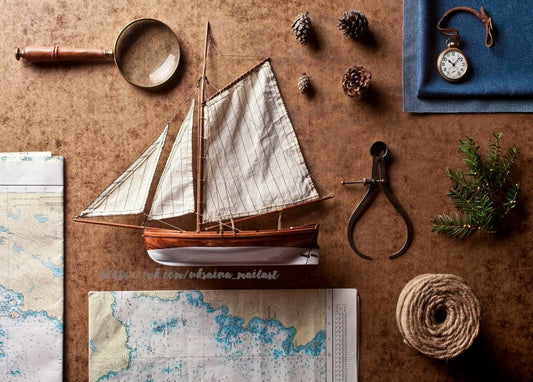 Modellsegelboot, Taschenuhr und Seekarten in einem Flatlay mit Tannenzapfen und Tannenzweig