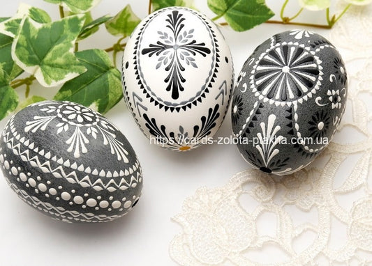 Black, white and grey pysanky eggs with intricate patterns among ivy leaves and lace