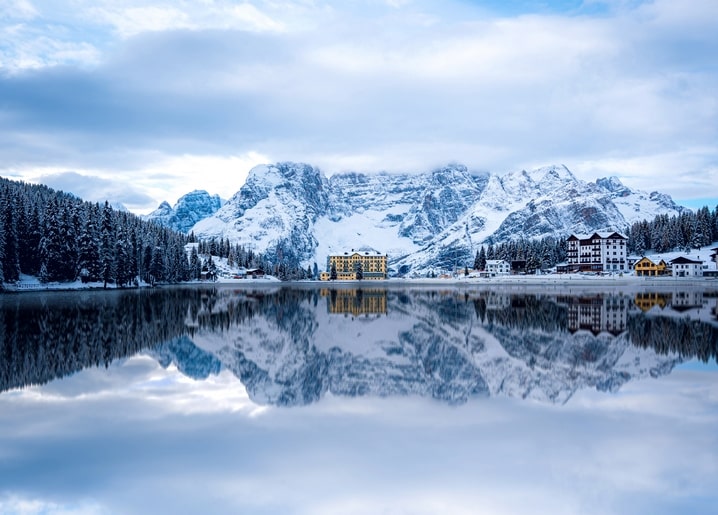 Snow-capped mountains and a lakeside village reflected in a still alpine lake