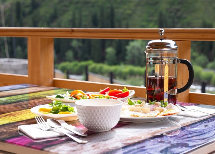 Frühstückstisch mit French-Press-Tee, Salaten und Käse auf einer Bergterrasse