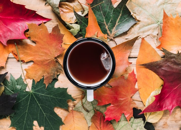 Black mug of tea resting on a bed of red, orange and green maple leaves