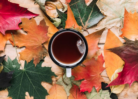 Black mug of tea resting on a bed of red, orange and green maple leaves