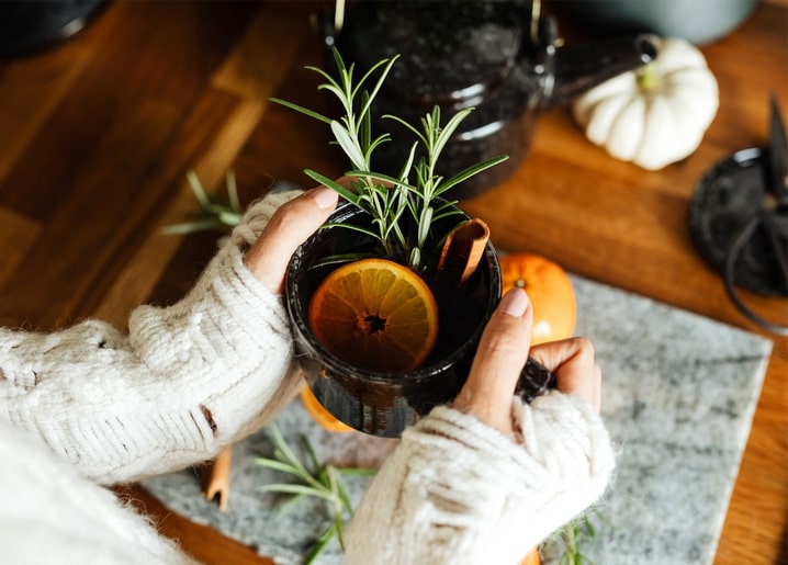 Hände halten einen Becher Glühwein mit Rosmarin, Orange und Zimt