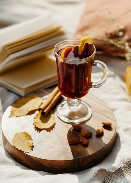 Mug of mulled wine with cinnamon and orange on a wooden board with almonds and autumn leaves.