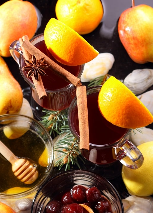 Two mugs of mulled wine garnished with orange, cinnamon sticks and star anise