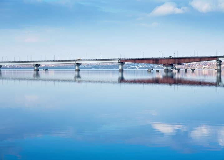 Довгий міст із ферменним прольотом, відображений у спокійній воді Південного Бугу