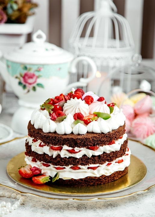 Naked chocolate cake with raspberries and meringue beside a vintage teapot