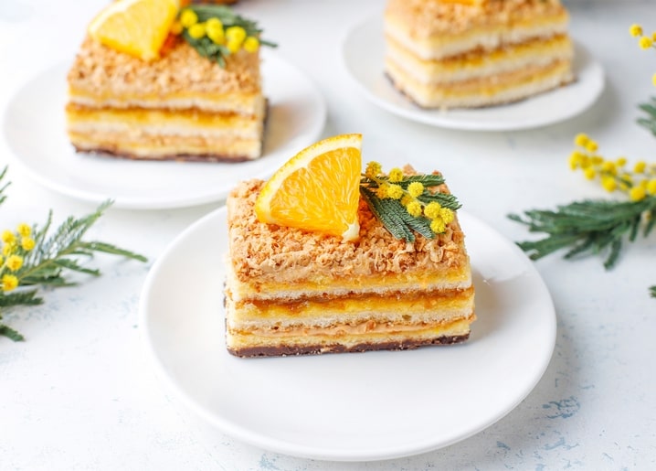 Stück Napoleon-Torte mit Orange und Mimosenzweig auf weißem Teller