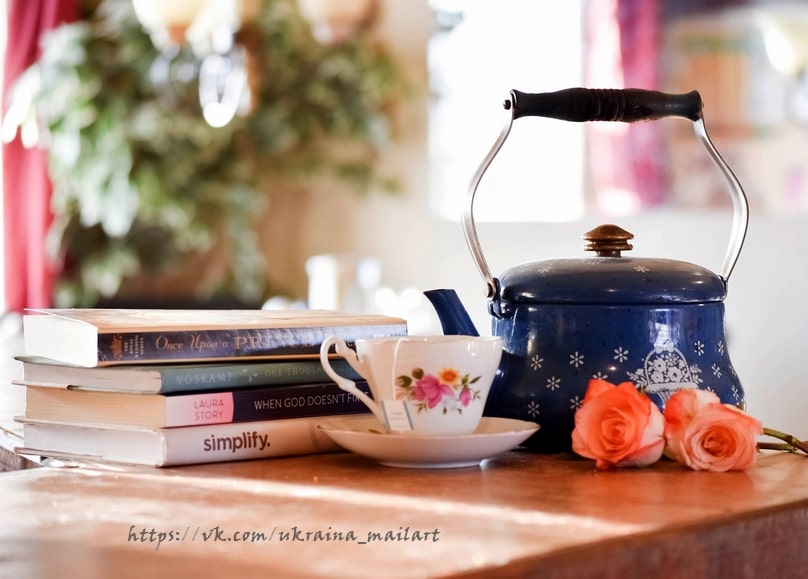 Blauer Emaille-Teekessel mit Rosen-Teetasse, Büchern und frischen Rosen auf einem Holztisch