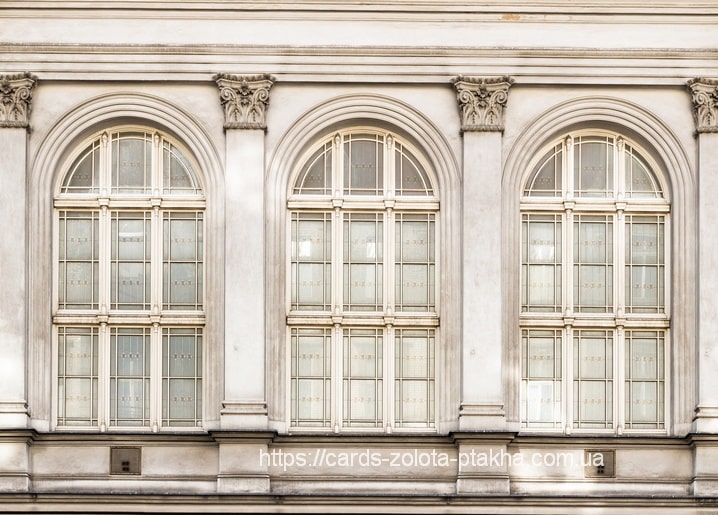 Drei hohe Bogenfenster mit schmiedeeisernen Gittern an einer hellen neoklassizistischen Fassade