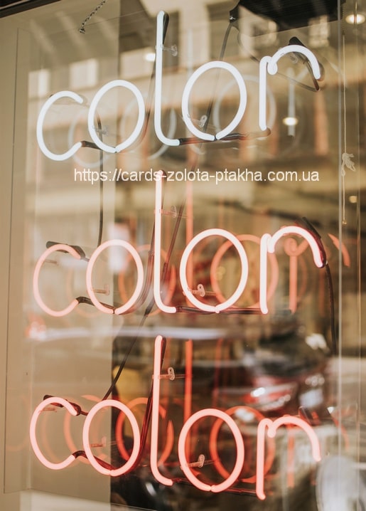 Dreifacher Neon-Schriftzug „color“ in Weiß und Korallrot hinter einem Schaufenster bei Nacht