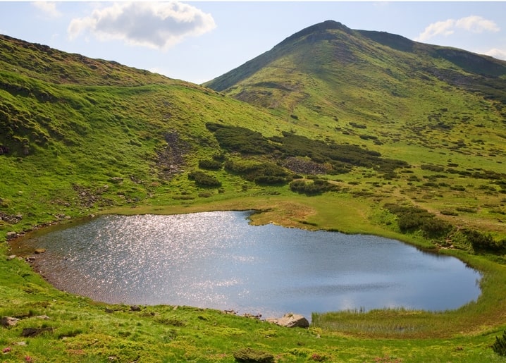 Nesamovyte Lake reflecting the sky beneath a green Carpathian mountain slope