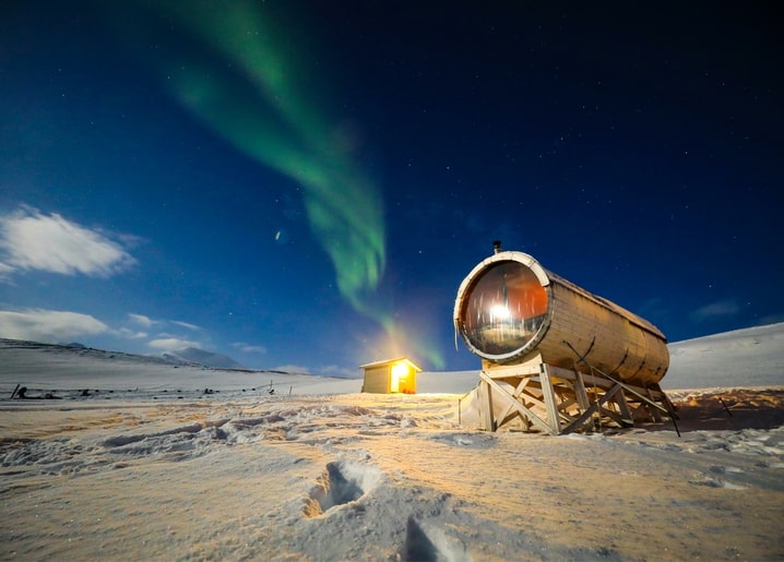 Nordlicht über einer schneebedeckten Fass-Sauna bei Nacht