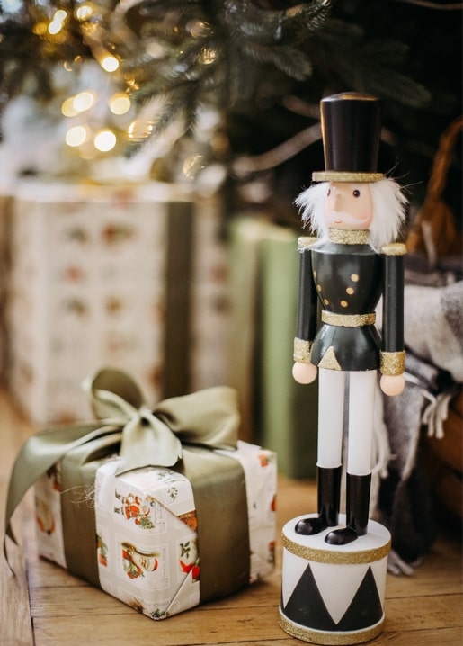 Wooden nutcracker figurine standing beside a ribbon-tied Christmas gift