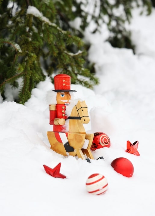 Hölzerner Nussknacker auf einem Schaukelpferd im Schnee, umgeben von Weihnachtsschmuck
