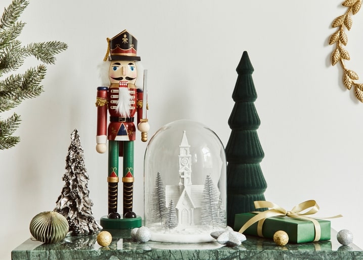 Wooden nutcracker figurine beside a glass snow globe with a miniature church and Christmas trees